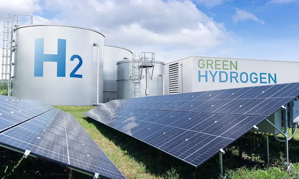 H2貯蔵タンクとグリーン水素製造ビルがある産業プラント、曇り空の下のソーラーパネル畑の前。