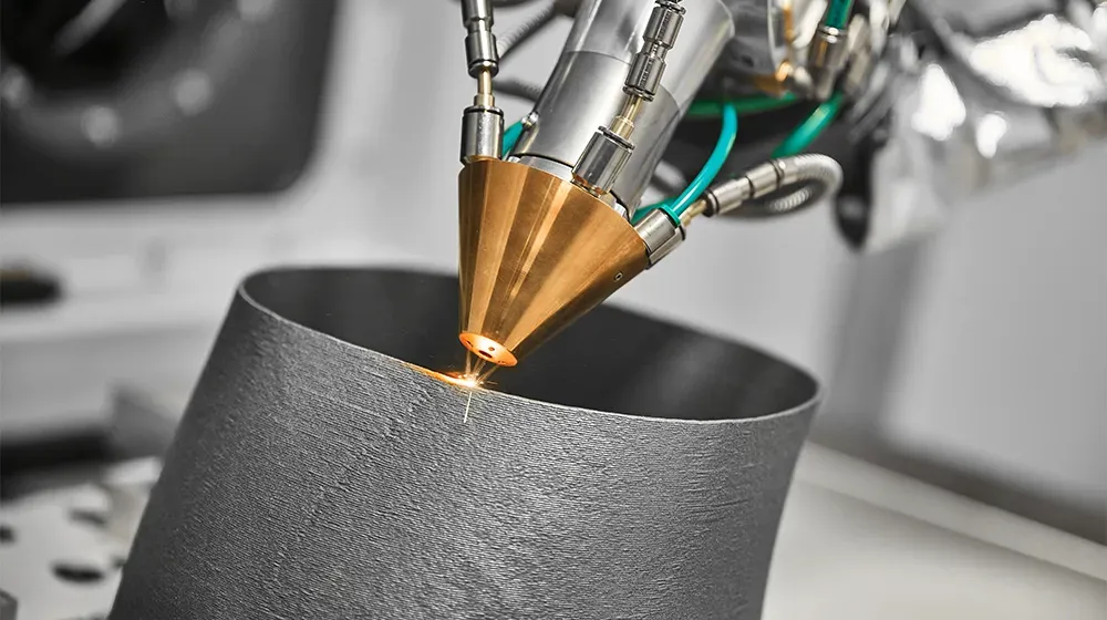 産業用3Dプリンターヘッドのクローズアップ。レーザーで金属粉末を溶融し、円筒形の部品を一層ずつ製造している。材料が堆積する際に火花が散っている。