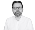 Black and white headshot of Tadeusz Dyduch, CEO of Manufacturo. He is wearing glasses and a white collared shirt and has a beard.
